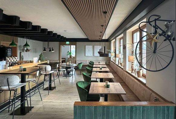 Een modern restaurant met een gezellige sfeer. Er zijn houten panelen, groene stoelen en decoratieve elementen aan de muur.