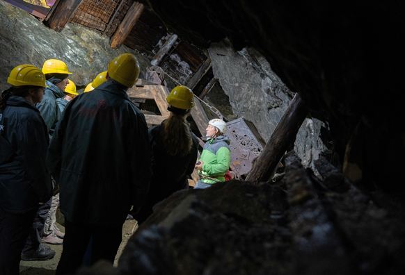 A group of people wearing hard hats stands in a cave. In the foreground, someone is explaining something to the others.