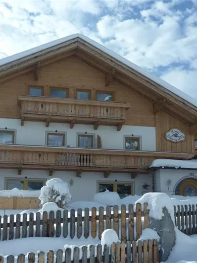 Ein charmantes Hotel im Schnee mit einem traditionellen Holzdesign. Die Umgebung ist winterlich und malerisch, umgeben von Bergen.