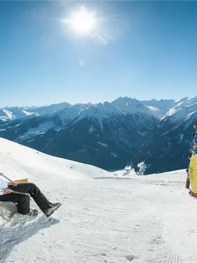 Een zonnige skiday in de bergen met met sneeuw bedekte hellingen. Twee skiers helpen een gewonde sporter op een helling.