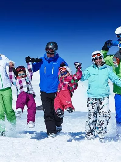 Een groep mensen in de sneeuw die vrolijk samen speelt. Ze dragen kleurrijke skikleding en genieten van de zonnige dag in de bergen.