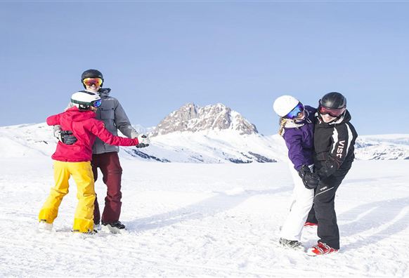 Two couples enjoy winter sports in the snowy mountains. They are wearing ski equipment and having fun in the sunny, winter landscape.