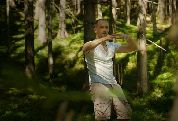 Zwei Personen machen Yoga am Ufer eines Sees. Im Hintergrund sind Berge und Boote sichtbar.