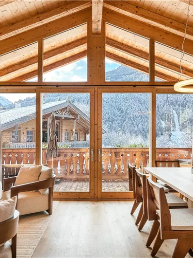 Ein modernes Wohnzimmer mit großen Fenstern und einem herrlichen Blick auf die Berge. Die Einrichtung ist hell und einladend, mit einem Esstisch und gemütlichen Möbeln.