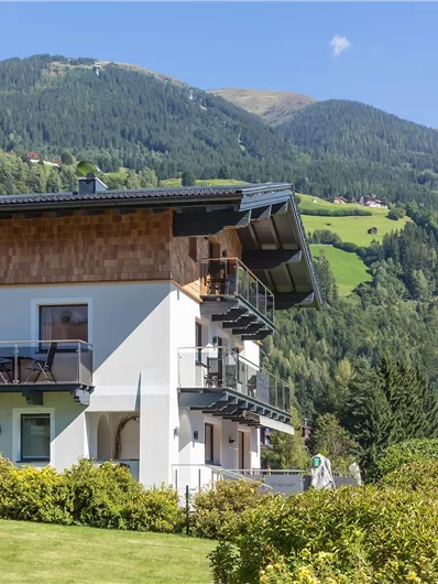 Een modern huis in de Oostenrijkse bergen, omringd door groene weilanden. Op de achtergrond zijn hoge bergen en een heldere blauwe lucht te zien.