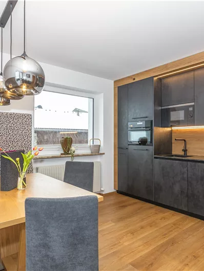 Een moderne keuken met elegante zwarte meubels en warme houten elementen. Een eethoek met een tafel en comfortabele stoelen completeert het gezellige ontwerp.