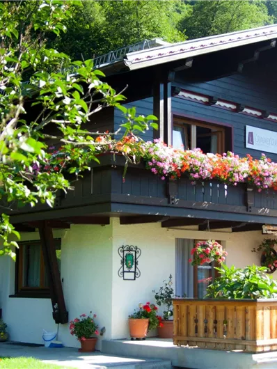 Een gezellig houten huis met een balkon vol bloeiende bloemen. De omgeving is groen en uitnodigend.