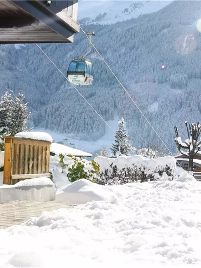 Een besneeuwde tuin met uitzicht op een berglandschap. Een bergbaan zweeft boven de witte sneeuwbedekking.