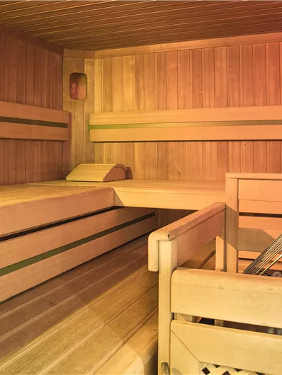 Ein gemütlicher Sauna-Raum aus Holz mit Bänken und einer angenehmen Atmosphäre. Die warmen Farben laden zum Entspannen ein.