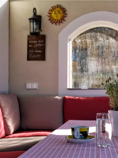 A cozy spot with a red sofa and a table. In the background, there is a decorative wall with a window and plants.
