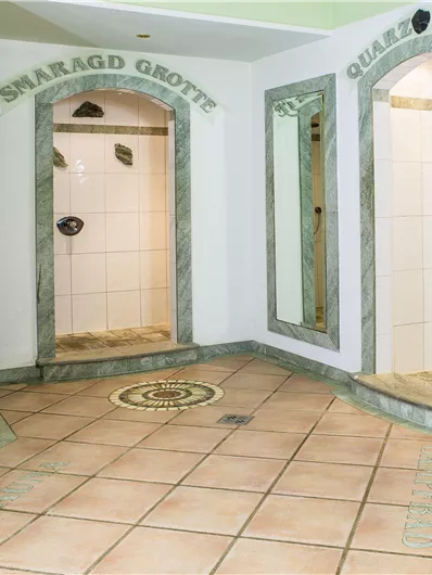 Ein eleganter Wellnessbereich mit mehreren Duschkabinen in einer modernen Einrichtung. Die Wände sind in sanften Farben gehalten und mit Marmorakzenten verziert.