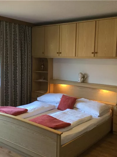 Ein gemütliches Schlafzimmer mit zwei Einzelbetten und Holzmöbeln. Das Fenster lässt viel Tageslicht hereinfliessen.