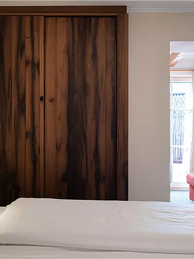 Ein modernes Schlafzimmer mit einem komfortablen Bett und einem Holzschrank. Im Hintergrund ist ein helles Sofa und ein Fenster zu sehen.