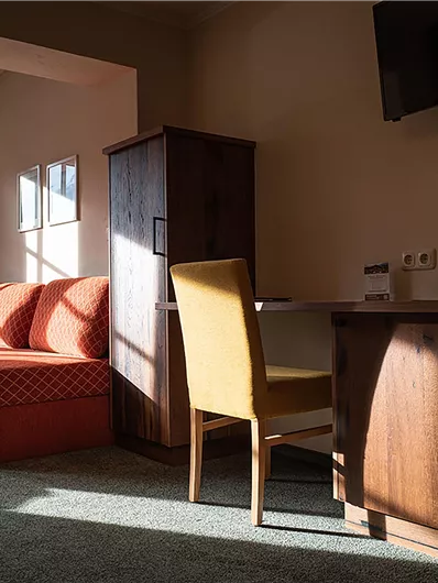 Ein gemütliches Zimmer mit einem roten Sofa und einem Schreibtisch. Der Raum hat große Fenster, die viel Tageslicht hereinlassen.