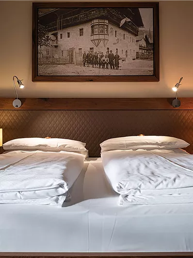 Ein gemütliches Zimmer mit zwei Betten und einem Holzkopfteil. Im Hintergrund hängt ein historisches Foto an der Wand.