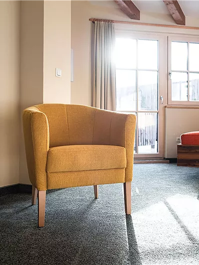 Ein gemütlicher Raum mit einem gelben Sessel und einem roten Sofa. Das Licht scheint durch das Fenster und schafft eine einladende Atmosphäre.