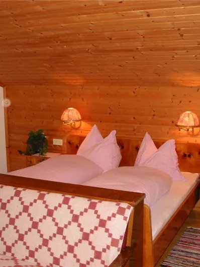 Een gezellige slaapkamer met houten wanden en plafond. Twee bedden met paarse kussens en zachte verlichting zorgen voor een uitnodigende sfeer.