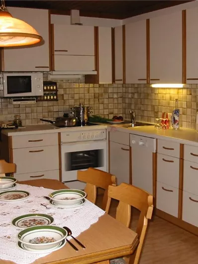 Een gezellige keuken met houten kasten en een eettafel. Op de tafel staan kommen en bestek, terwijl de ruimte goed verlicht is.