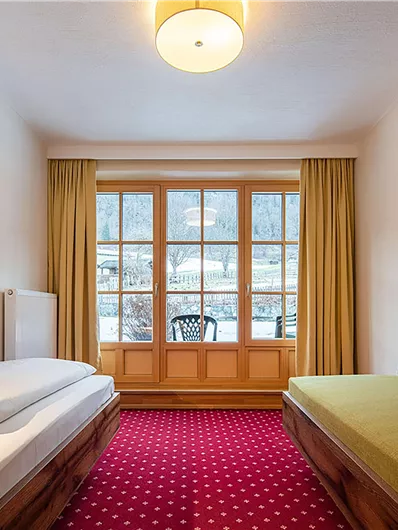 Ein gemütliches Hotelzimmer mit zwei Betten und einem großen Fenster. Der Boden ist mit rotem Teppich ausgelegt und die Wände sind hell gestrichen.