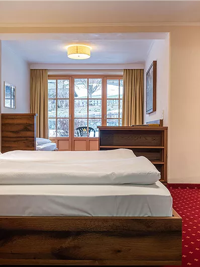Ein gemütliches Hotelzimmer mit einem großen Bett und einem Schreibtisch. Große Fenster lassen viel Tageslicht herein.