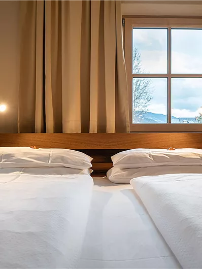 Ein gemütliches Schlafzimmer mit einem Doppelbett und zwei Nachttischen. Der Blick aus dem Fenster zeigt einen bewölkten Himmel.