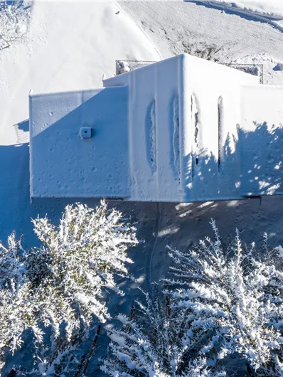 Een modern huis, volledig bedekt met sneeuw, staat in een winterlandschap. Omringd door met sneeuw bedekte bomen straalt de scène rust en koude uit.