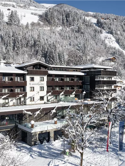 Een sfeervol hotel in een besneeuwd berglandschap. De omgeving wordt gekenmerkt door met sneeuw bedekte bomen en een helderblauwe lucht.