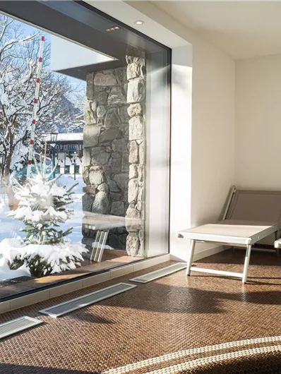Een gezellige kamer met twee ligbedden en grote ramen. Buiten sneeuwt het en het landschap is bedekt met sneeuw.