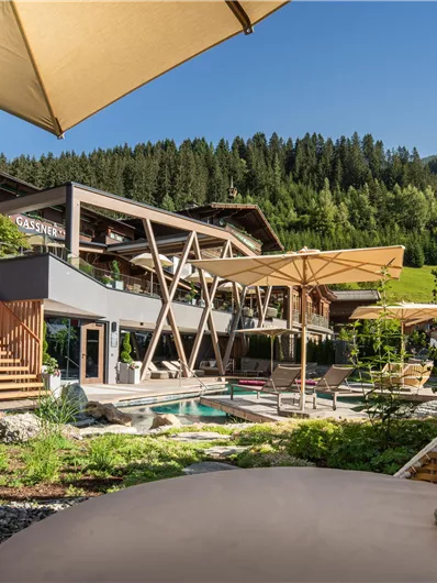 Ein modernes Hotel mit stilvollen Terrassen und einem Schwimmbecken. Die Umgebung ist grün und von Bäumen umgeben, ideal für entspannte Aufenthalte.
