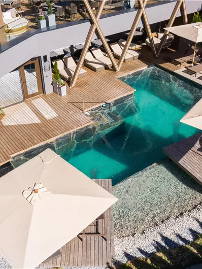 Ein moderner Außenbereich mit einem glitzernden Pool und Sonnenliegen. Sonnenschirme bieten Schatten, umgeben von stilvollen Holzdeck und Gartenlandschaft.