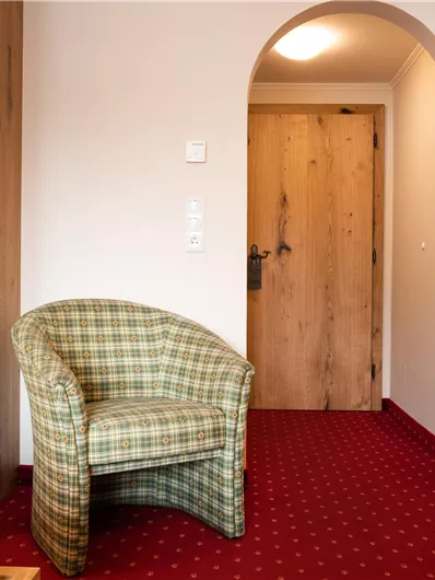 Ein gemütlicher Raum mit einem karierten Stuhl und einem Holztür in natürlichem Design. Der Boden ist mit rotem Teppich ausgelegt.