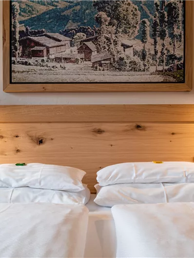 Ein gemütliches Schlafzimmer mit zwei Betten und warmen Holzelementen. An der Wand hängt ein Bild einer ländlichen Landschaft.