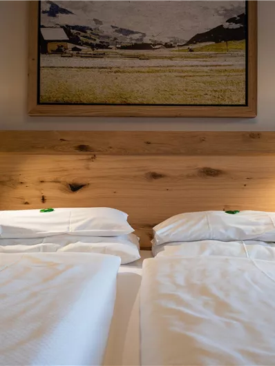 Ein gemütliches Schlafzimmer mit zwei Einzelbetten und einem Holzkopfteil. Sanfte Beleuchtung und ein Landschaftsbild an der Wand sorgen für eine einladende Atmosphäre.