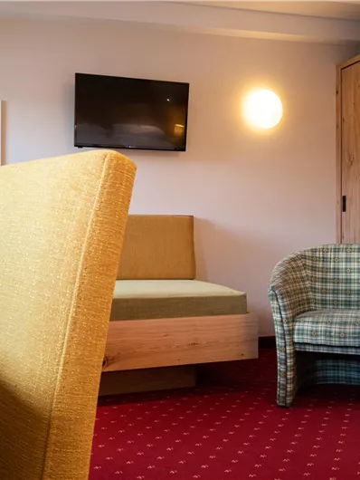 Ein modernes Zimmer mit einem Fernseher, einem Sessel und einer Couch. Der Boden ist rot und es gibt einen großen Schrank aus Holz.