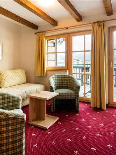 Ein gemütliches Wohnzimmer mit zwei karierten Sesseln und einem Sofa. Große Fenster lassen viel Licht herein und bieten einen Blick nach draußen.