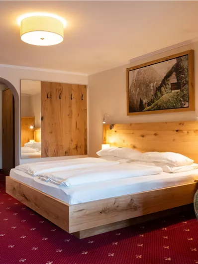 Ein gemütliches Hotelzimmer mit einem großen Doppelbett und Holzdetails. In der Ecke steht ein komfortabler Sessel und es gibt ein Bild an der Wand.