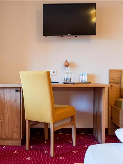 Ein gemütliches Zimmer mit einem Tisch, einem Stuhl und einem Fernseher an der Wand. Die Wände sind hell, und das Ambiente wirkt einladend.