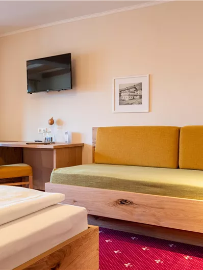 Ein gemütliches Zimmer mit einem Holzbett und einer grünen Couch. An der Wand hängt ein Fernseher und es gibt einen Schreibtisch mit einem Stuhl.