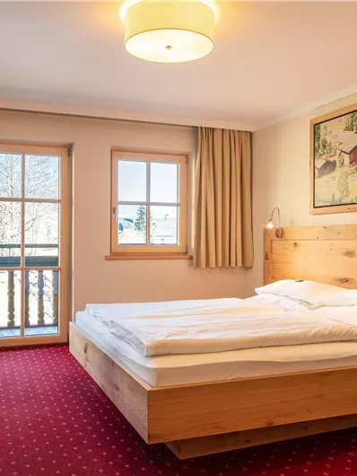 Ein modernes Schlafzimmer mit einem Doppelbett und Holzdetails. Es gibt ein Fenster mit Blick nach draußen und einen Schreibtisch mit einem Stuhl.