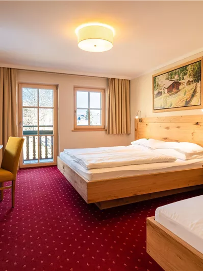 Ein gemütliches Hotelzimmer mit zwei Betten, Holzmöbeln und rotem Teppich. Der Raum hat ein Fenster mit Aussicht und eine angenehme Beleuchtung.