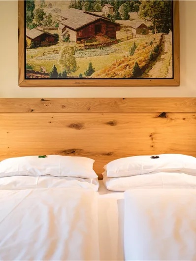 Ein gemütliches Schlafzimmer mit zwei getrennten Betten und einer Holzwand. Über dem Bett hängt ein eingerahmtes Landschaftsbild.