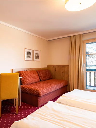 Ein bequemes Hotelzimmer mit zwei Einzelbetten und einem Sofa. Der Raum hat einen Fernseher, einen Schreibtisch und Zugang zu einem Balkon mit Blick nach draußen.
