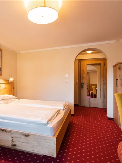 Ein gemütliches Schlafzimmer mit einem großen Bett und einem roten Teppich. Außerdem gibt es einen Schreibtisch und einen Fernseher an der Wand.