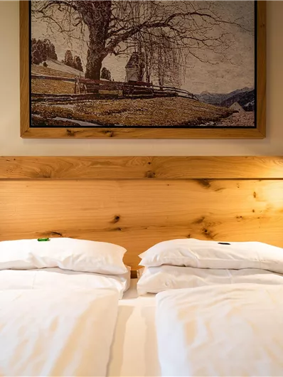 Ein gemütliches Schlafzimmer mit zwei Einzelbetten und einer Holzbettenkopfzeile. An der Wand hängt ein Landschaftsgemälde, das eine ruhige Atmosphäre schafft.