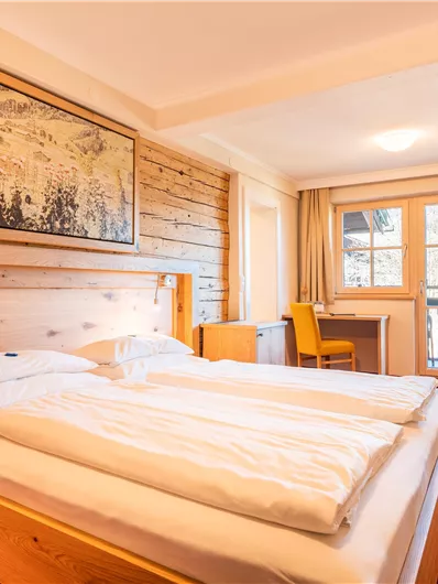 Ein gemütliches Hotelzimmer mit einem Doppelbett und Holzverkleidung. Es gibt einen Fernseher, einen Sessel und einen Blick auf den Balkon.