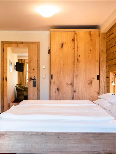 Ein gemütliches Schlafzimmer mit einem Doppelbett und Holzdetails. Die Wände sind hell, und es gibt einen Zugang zu einem anderen Raum.