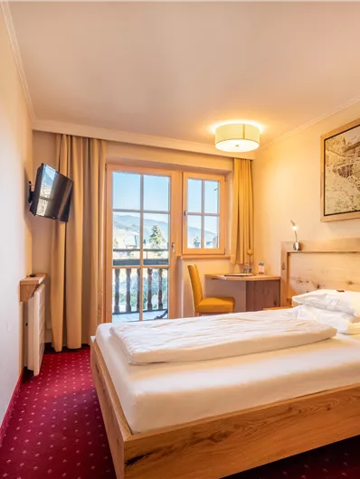 Ein gemütliches Hotelzimmer mit einem Doppelbett und einem Tisch. Große Fenster lassen viel Licht herein und bieten einen Blick auf die Umgebung.