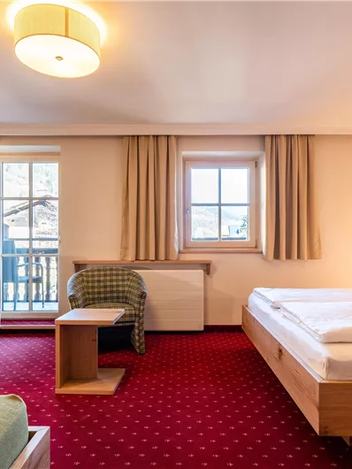 Ein helles Hotelzimmer mit zwei Betten, einem Tisch und einem Fernseher. Es gibt große Fenster und eine gemütliche Atmosphäre.