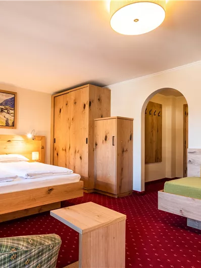 Ein gemütliches Hotelzimmer mit einem Doppelbett und einer Sitzecke. Die Holzverkleidung und der Teppich schaffen eine warme Atmosphäre.