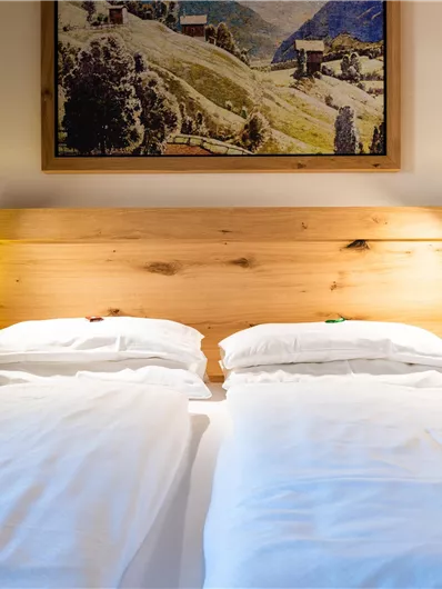 Ein gemütliches Schlafzimmer mit zwei Betten und einem Holzheadboard. An der Wand hängt ein Landschaftsgemälde, und beside den Betten stehen kleine Lampen.